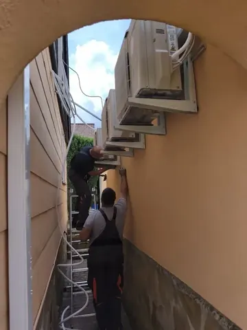 Zwei Mitarbeiter von OK Bau UG montieren Klimageräte an einer Hauswand.