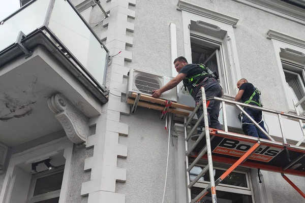 Monteure installieren ein Klimagerät an der Hausfassade